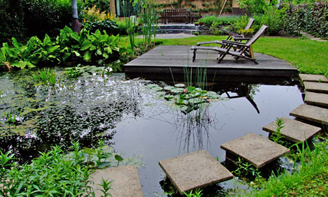 Tuin met vijver, stapstenen en een houten vlonder met ligstoelen, aangelegd door De Wyngaerd